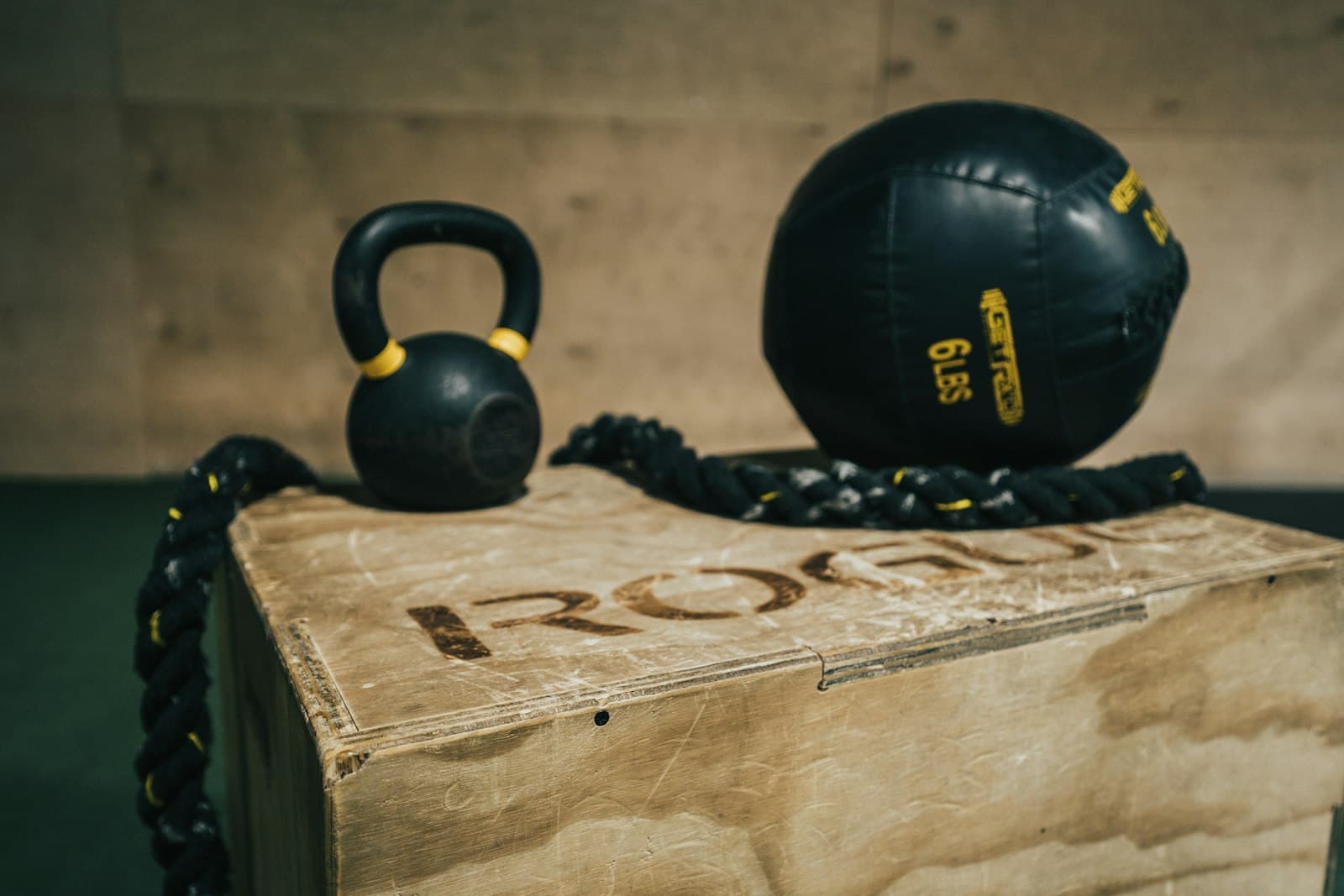 Kettlebell en medicine ball op een houten plyobox, met een battle rope ernaast