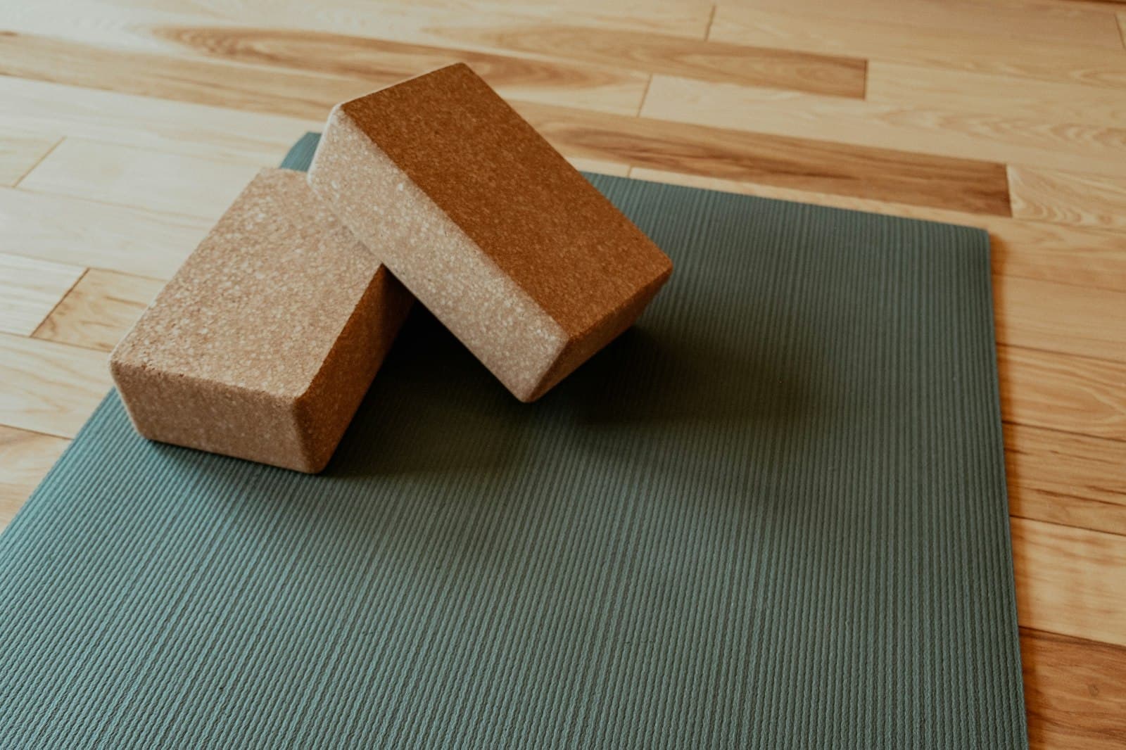 Twee kurken yogablokken op een groene yogamat op een houten vloer