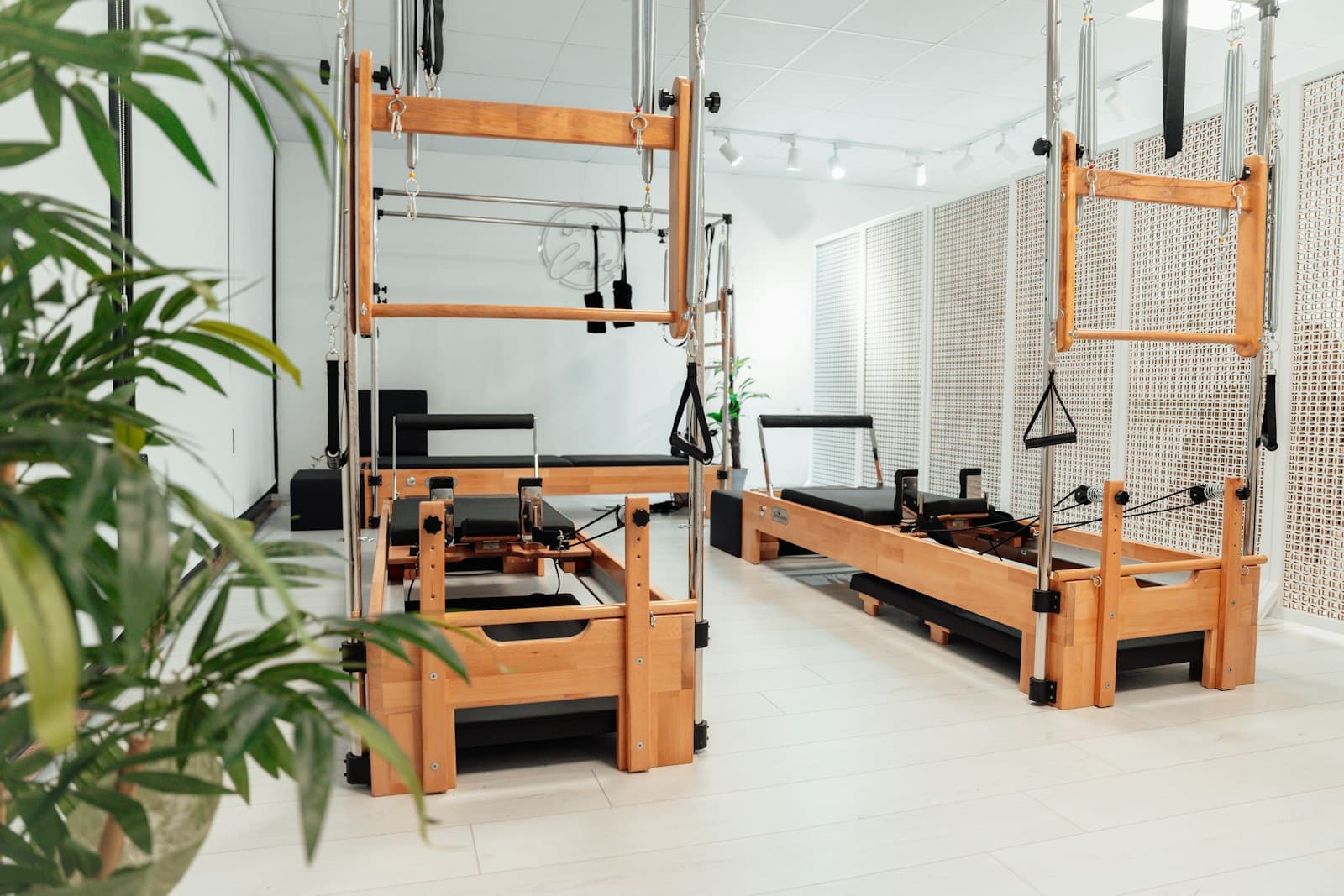 Pilatesstudio met houten reformers en een cadillac, met planten op de voorgrond